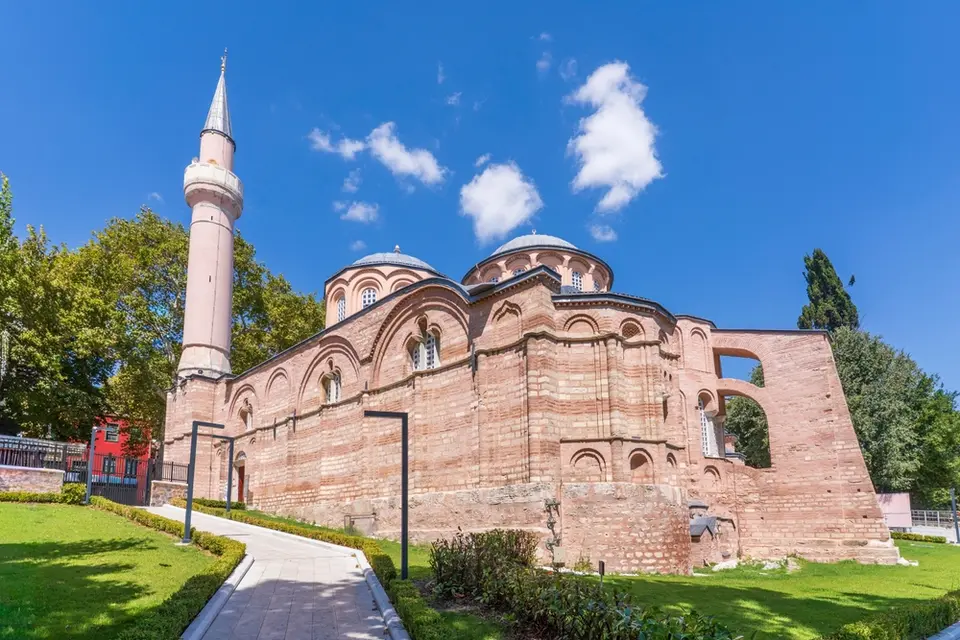Path through a lawn leading to a brick church with domes and a minaret on the left