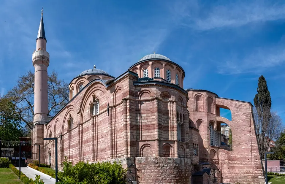 Brick and stone church with a central dome, smaller domes and a single minaret under a blue sky